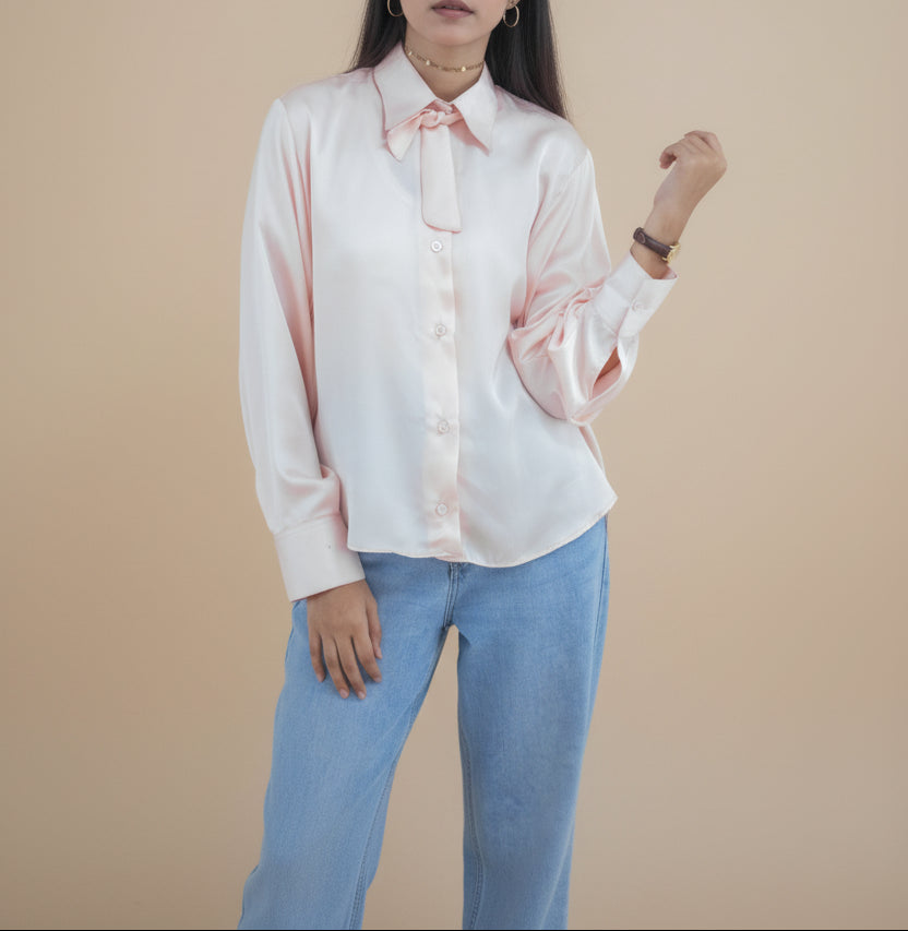Person wearing a light pink blouse and blue jeans against a beige background
