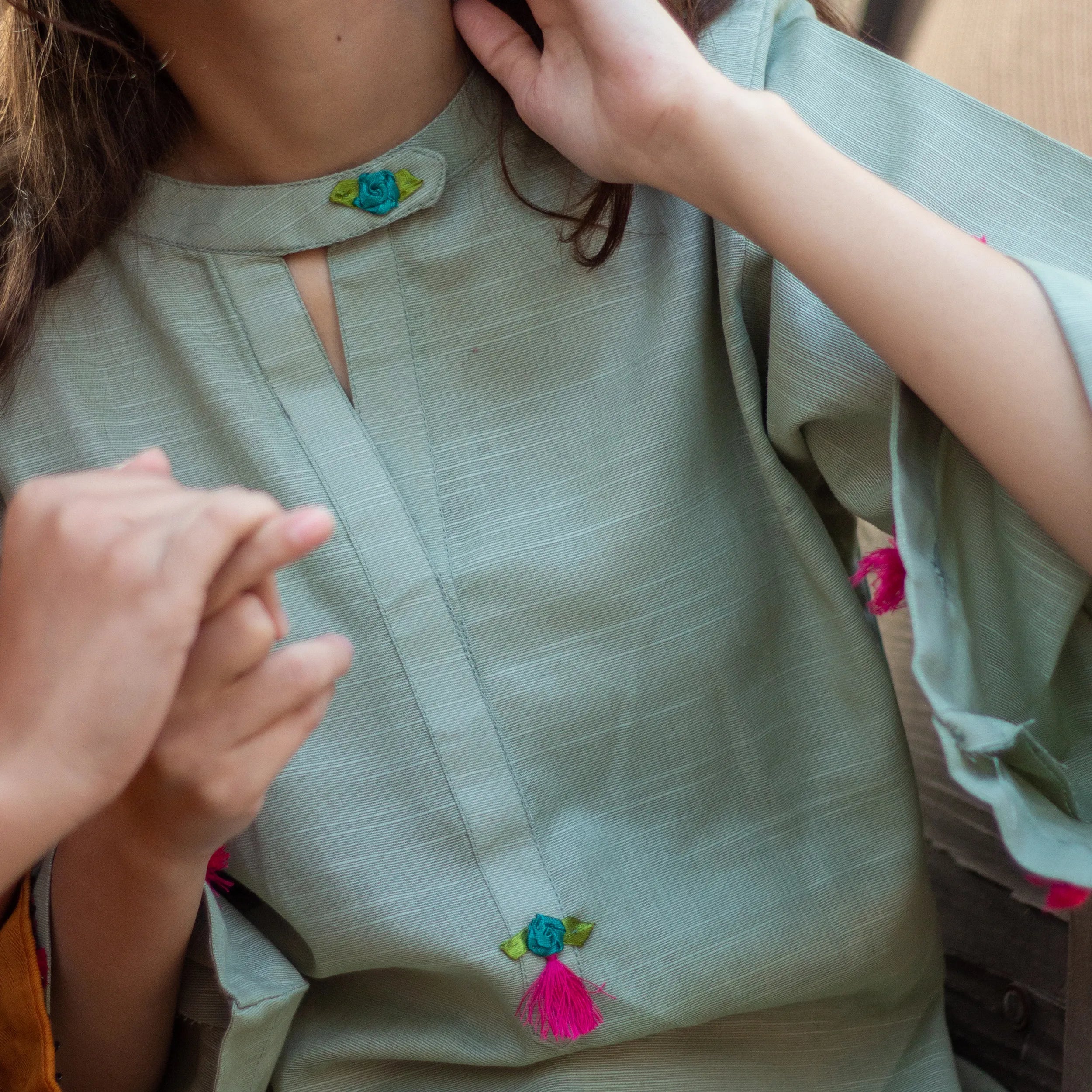 Light green blouse with pink tassels worn by a girl, close-up view.